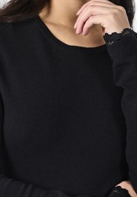 Pull en tricot noir avec un col rond et des accents en dentelle sur les poignets. Texture lisse, coupe ajustée et manches longues.