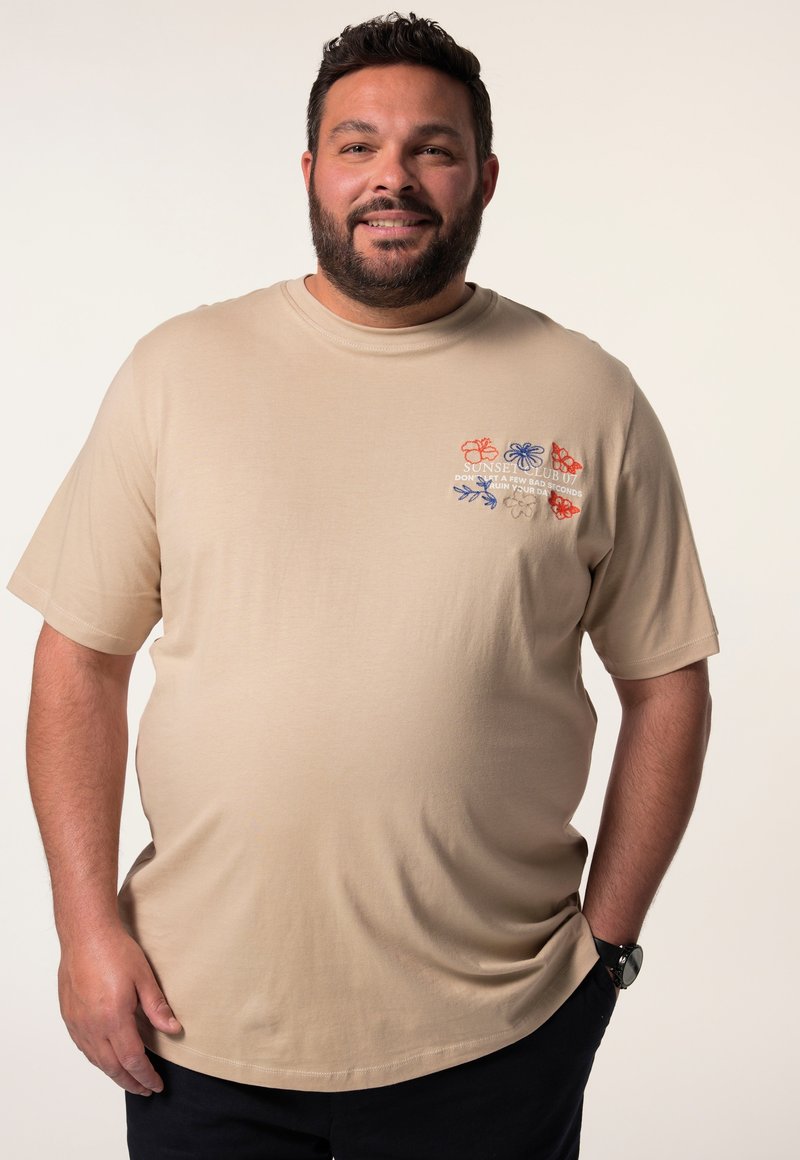Béžové bavlněné tričko s barevným květinovým vyšíváním na levé hrudi. Krátké rukávy, kulatý výstřih, měkká struktura a volný střih.