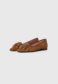 Brown suede flat shoes with low heels, adorned with large floral appliques and small metallic studs on the toes.