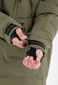 Oliven grøn pufferjakke med sorte håndledsmanchetter; fremhæver velcro-lukninger og en tætsiddende pasform omkring hænderne. Belagt, polstret materiale.
