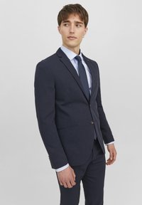 Marineblå drakt med slim fit, med enkel knapplukking, notch revers og to frontlommer. Kombinert med en lys blå skjorte og slips.