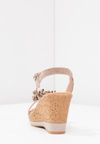 Sandalia de cuña beige con tacón de corcho, acento de tejido rizado en la correa y cierre de hebilla en el tobillo. Textura suave y diseño abierto.