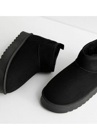 Czarne botki za kostkę wykonane z gładkiego sztucznego zamszu, z teksturowaną gumową podeszwą. Posiadają okrągły czubek i uchwyt do łatwego zakładania.
