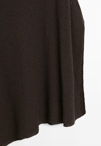 Mørkebrunt strikket stof med en løs, let tekstureret vævning og en blød fald mod en hvid baggrund.