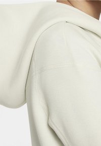 Sweat à capuche beige clair avec une texture douce. Comprend une capuche arrondie, des épaules sans coutures et des coutures visibles le long des surpiqûres.