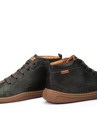 Zapatillas casuales de cuero negro con suelas y cordones de goma marrón, con etiquetas de la marca Pikolinos en la lengüeta y en el lateral.
