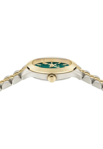 Sudraba un zelta toņa rokas pulkstenis ar apaļu zaļu ciparnīcu, trim rādītājiem, zelta atzīmēm un rievotu krānu, kam ir izliekts nerūsējošā tērauda korpuss.