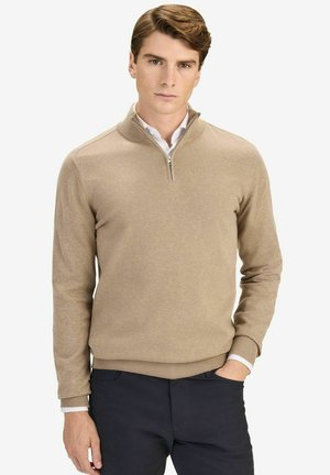 Beige Halb-Zip-Pullover aus weichem Strickstoff. Mit gerippten Bündchen und Saum, übereinander getragen mit einem weißen Hemd und kombiniert mit dunklen Hosen.