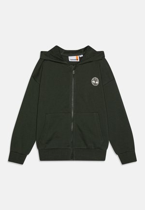 Mørkegrønn hettejakke med glidelås laget av myk stoff, med en frontlomme og et sirkulært logo på venstre bryst. Ribbestrikkede mansjetter og kant.