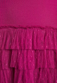 Tissu rose vif avec une partie supérieure en tricot côtelé et des volants superposés en tulle transparent en dessous.