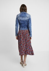 Denim jacket with a faded blue finish, fitted shape, and button accents, paired with a floral patterned red and blue midi skirt.
