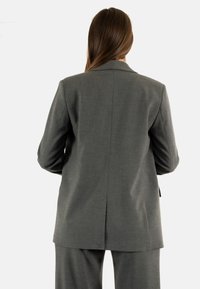 Blazer grigio su misura con colletto a V, spacco sul retro e superficie liscia. Si abbina a pantaloni coordinati per un look completo.