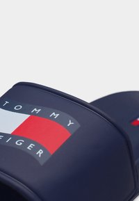 Κοντινό πλάνο της σαγιονάρας σε ναυτικό μπλε χρώμα με το λογότυπο Tommy Hilfiger σε κόκκινο, λευκό και μπλε στη λουρίδα.