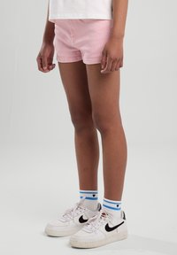 Pink cotton shorts with front pockets, paired with white sneakers and blue-striped socks. Shorts have a fitted design and are mid-thigh length.