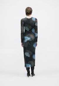 Černé šaty s dlouhým rukávem a modrým květinovým vzorem, vyrobené z průsvitné látky, s přiléhavým střihem a délkou do poloviny lýtek, doplněné černými botami na podpatku.