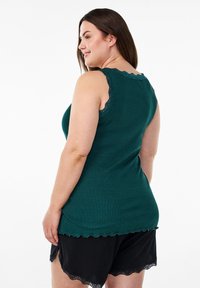 Zelený bezrukávový top s čipkovým lemovaním, ryhovanou textúrou a zakriveným dolným okrajom, spárovaný s čiernymi šortkami s vyrezávaným čipkovým zdobením.