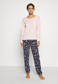 Lichtroze langetermijn top met een borstzak, gecombineerd met marineblauwe broek met bloemenprint, voorzien van een elastische tailleband en taps toelopende broekspijpen.