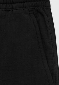 Primer plano de tela negra, mostrando detalles texturizados y costuras cosidas, probablemente de un par de pantalones o pantalones cortos.