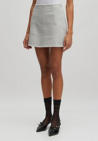Grijze katoenen minirok van een katoenmix met verticale naden. Draagt met zwarte doorschijnende sokken en schoenen van patentieler met een spitse neus.