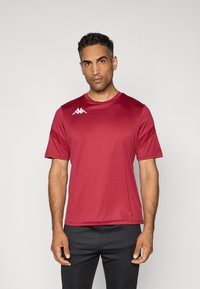 Rode sport t-shirt van glad, ademend stof. Bevat een ronde hals en korte mouwen met een wit logo op de linkerschouder.