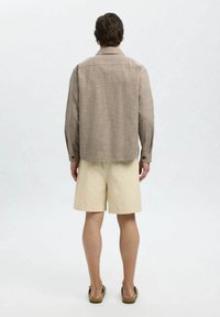 Brunternet knap-op skjorte med en afslappet pasform, kombineret med beige shorts. Har lange ærmer, knapmanchetter og en lige kant.