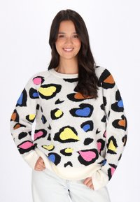 Pull en tissu doux, avec une base blanche ornée de formes abstraites colorées en rose, jaune, bleu et orange, et des poignets côtelés.