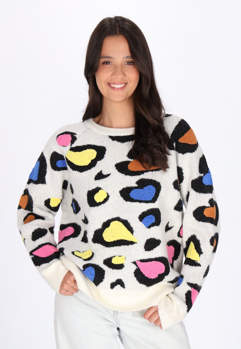Pull en tissu doux, avec une base blanche ornée de formes abstraites colorées en rose, jaune, bleu et orange, et des poignets côtelés.
