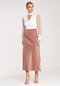 Langes Kleid mit einem weißen Oberteil, das über einen Schlüsselloch-Ausschnitt und transparente Puffärmel verfügt. Der Rock ist in einem glatten, glänzenden Rosaton gehalten.