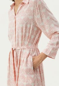 Robe rose à motifs avec col, manches longues et taille ceinturée. Fabriquée en tissu léger avec des motifs abstraits et des poches latérales.