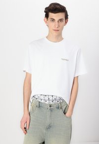 Hvit bomulls t-skjorte med en liten gulllogo på brystet, paret med lyseblå denimshorts med en lett falmet tekstur.
