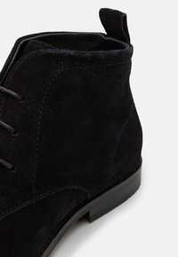 Bottines en daim noir avec un bout arrondi, des lacets et une languette. Présente une semelle en caoutchouc lisse et des coutures visibles le long des coutures.