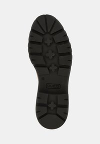 Suela de zapato de goma negra con un dibujo de patrón, con detalles en forma de cruz y un logo de "GUESS". Texturizada para proporcionar agarre y estabilidad.