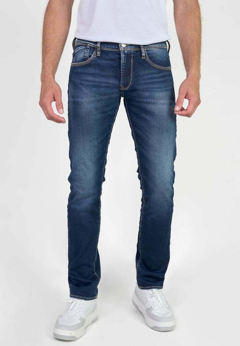 Jeans de hombre de denim azul oscuro con corte recto, ligero desvanecimiento, costuras naranjas y cinco bolsillos. Llevados con zapatillas blancas.