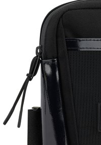 Borsa in tessuto nera con un accento nero lucido. Presenta una superficie texturizzata, una cerniera liscia e un sottile dettaglio della tracolla. Design compatto.