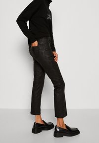 Svarta faux läderbyxor med ett ormskinnsmönster, rak passform, ankellång, tillsammans med svarta slip-on loafers.