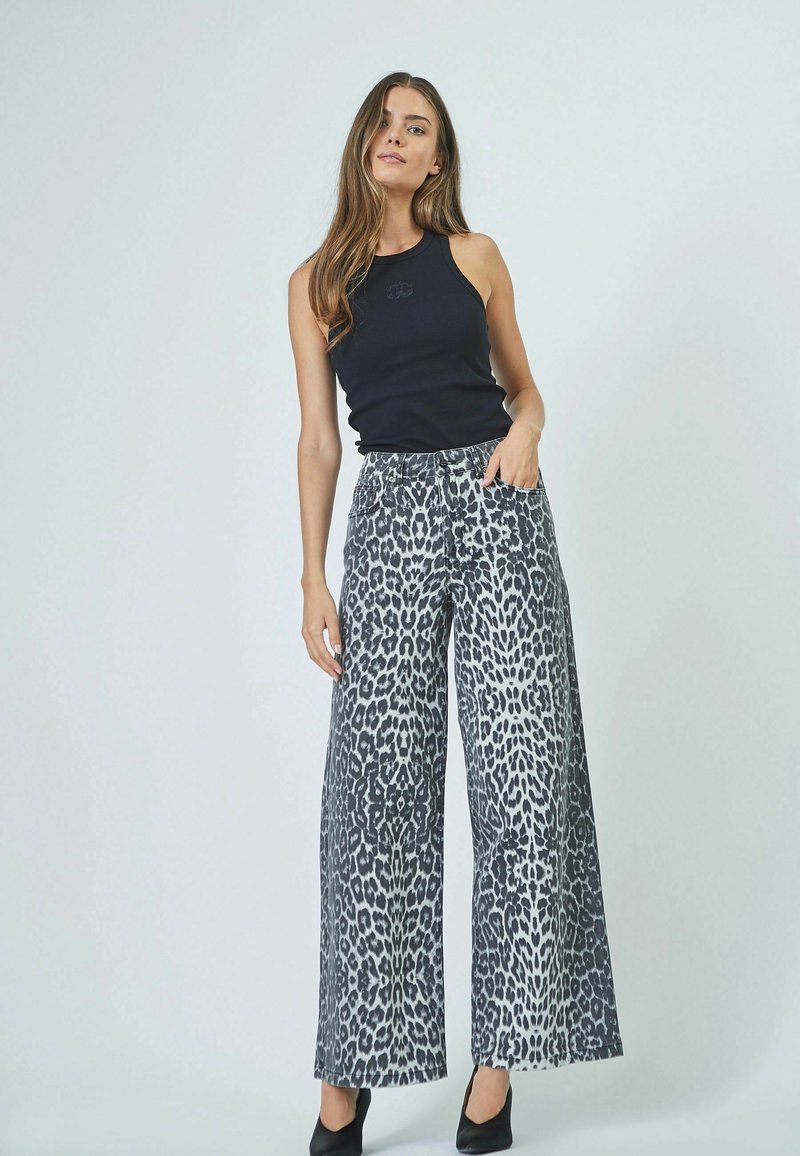 Leopard print wide-leg pants in grey and black, made of denim. Features a high waist and side pockets. Paired with a black sleeveless top.