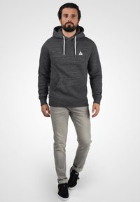 Sudadera gris oscuro con un acabado texturizado, ojales de metal y cordones. Combinada con jeans gris claro y zapatillas negras.