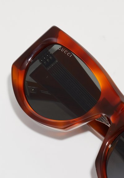 Gucci napszemüveg nagyméretű, szögletes teknősbéka mintás kerettel, sötét lencsékkel és a szárán lévő domború logóval. A belső felülete textúrált.
