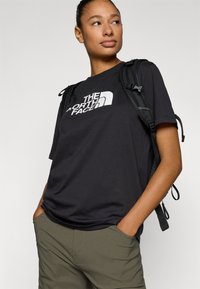 Μαύρο βαμβακερό μπλουζάκι με λευκό λογότυπο "The North Face". Φορεμένο με πράσινα cargo σορτς και μαύρο σακίδιο πλάτης με ρυθμιζόμενους ιμάντες.