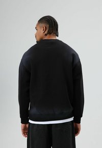 Zwarte trui met een ronde hals en verlaagde schoudernaden, met een gladde textuur en een licht verlopende zoom, gecombineerd met een donkere broek.