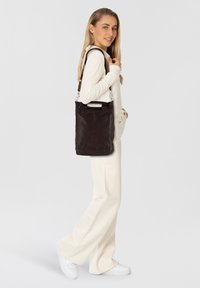 Borsa a mano in pelle marrone scuro con superficie texturizzata, dotata di un manico corto e di una lunga tracolla regolabile per maggiore versatilità.