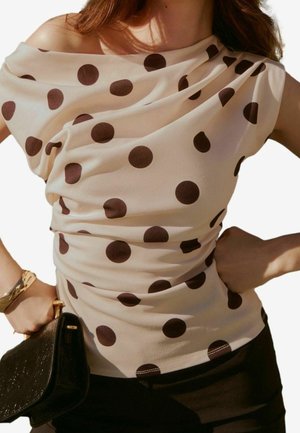 Beige Bluse mit Polka-Dots und drapiertem Off-Shoulder-Design. Mit dunklen braunen kreisförmigen Mustern, leichtem Stoff und figurnahem Schnitt.