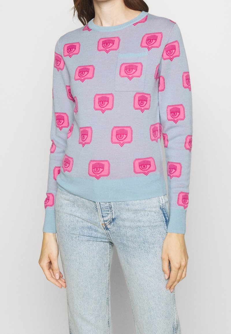 Ljusblå tröja med rosa grafiskt mönster. Har rund halsringning, långa ärmar och en bröstficka. Stickad tyg med mjuk textur.