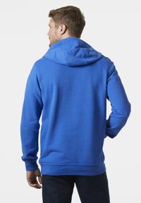 Modrá mikina s kapucí vyrobená z texturované látky, dlouhé rukávy a stahovací kapuce, z pohledu zezadu, s klasickým střihem a žebrovanými manžetami.