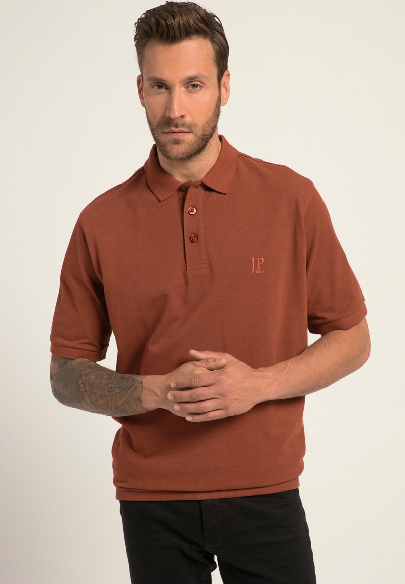 Rostfarbendes Poloshirt aus strukturiertem Stoff mit Kragen, drei Knöpfen und einem kleinen gestickten Logo auf der Brust.