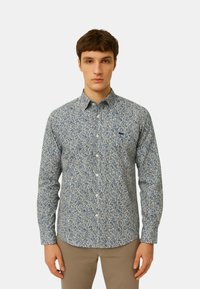 Camicia a maniche lunghe di colore blu chiaro con motivo floreale in blu scuro, colletto button-down e logo discreto sul petto. Materiale in cotone testurizzato.
