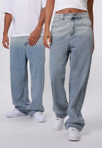 Lyseblå denim bukser med brede ben og bleget tekstur, fem lommer og knaplukning. Båret med hvide sneakers.