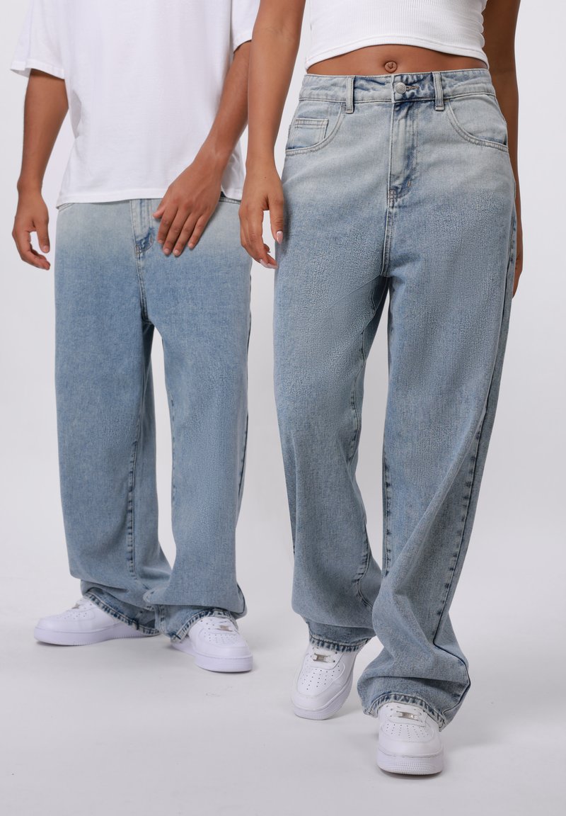 Lyseblå denim bukser med brede ben og bleget tekstur, fem lommer og knaplukning. Båret med hvide sneakers.