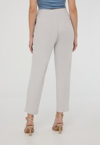 Pantaloni grigi chiari con vestibilità rilassata, vita elastica e due tasche posteriori, abbinati a tacchi beige con cinturino alla caviglia. Texture liscia.