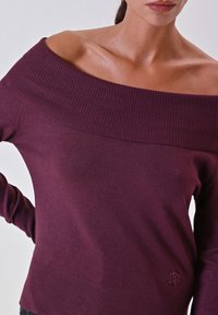 Bordeauxfarbenes Off-Shoulder-Sweater mit geripptem Kragen und glatter Textur. Mit langen Ärmeln und einem kleinen Logo an der Taille.